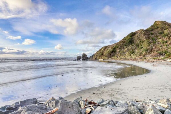 Ein Strand mit felsigem Vordergrund, einem Sandufer und einem Hügel mit spärlicher Vegetation.