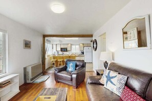 Un salon comprenant un canapé en cuir, un fauteuil en cuir et un coin repas avec des chaises en bois.