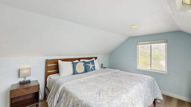 Quarto com uma cama de solteiro, mesa de cabeceira, janela e teto inclinado.