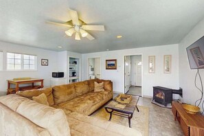 A living room with a large sofa, a coffee table, a ceiling fan, and a fireplace. - Seascape Home & Cottage (Trinidad)
