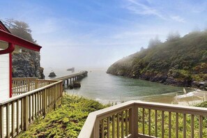 A coastal view with a wooden deck overlooking a calm sea, rocky cliffs, and a pier extending into the water. - Seascape Home & Cottage (Trinidad)