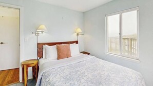 Quarto com cama, duas luminárias de cabeceira, uma janela com vista e uma porta.