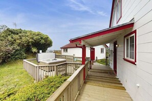 Une terrasse en bois mène à un bâtiment blanc orné de bordures rouges et comprend un espace couvert avec un jacuzzi.
