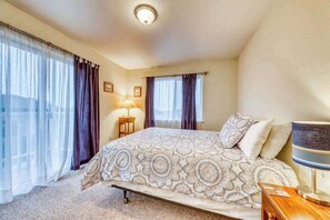 A hotel room with a large bed, two windows with curtains, a bedside lamp, and a small table. - Seventh Street Select (Eureka)