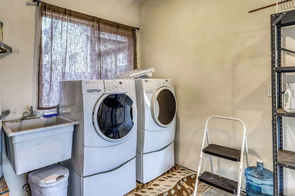 A laundry room with two stacked washing machines, a sink, a trash bin, and a water dispenser.
