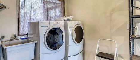 A laundry room with two stacked washing machines, a sink, a trash bin, and a water dispenser.