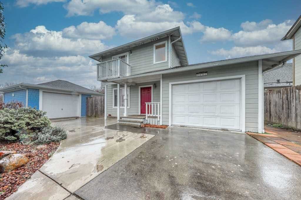 A two-story residential house with a front garage, a red door, and a small porch with a railing.