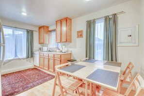 A compact kitchen with wooden cabinets, a dining table with chairs, and a patterned rug. - Seventh Street Select (Eureka)