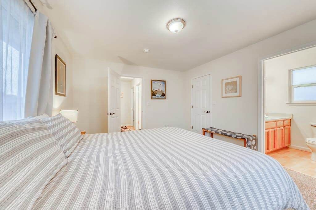 Une chambre à coucher avec un grand lit, une table de chevet, une chaise, une armoire et une salle de bain visible à travers une porte ouverte.