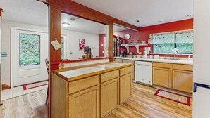 A kitchen with wooden cabinets, a white countertop, and a window with a view of greenery. - Peaceful Creekside - Tranquil Nature Retreat by the Water (Trinidad)