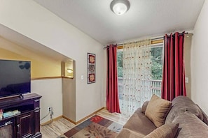 A living room with a television, a sofa, and a window with red curtains. - Peaceful Creekside - Tranquil Nature Retreat by the Water (Trinidad)