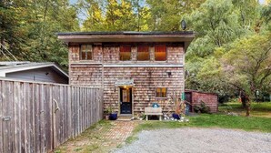 A two-story wooden cabin with a front porch, a small shed, and a fenced yard. - Peaceful Creekside - Tranquil Nature Retreat by the Water (Trinidad)
