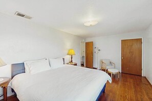 Une chambre d’hôtel avec un lit, une table de chevet, une lampe, une chaise et une porte en bois.