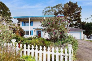 A two-story house with a white exterior and blue trim, surrounded by a white picket fence and lush vegetation. - Eureka Charmer - Cozy Historic Getaway in the Heart of Town (Eureka)