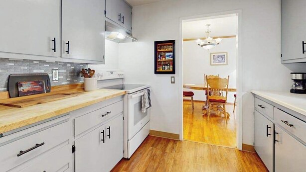 A kitchen with white cabinets, a wooden countertop, and a dining area with a chair and table. - Eureka Charmer - Cozy Historic Getaway in the Heart of Town (Eureka)