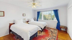 A room with two beds, a ceiling fan, a window with blue curtains, and a small table with a chair. - Eureka Charmer - Cozy Historic Getaway in the Heart of Town (Eureka)
