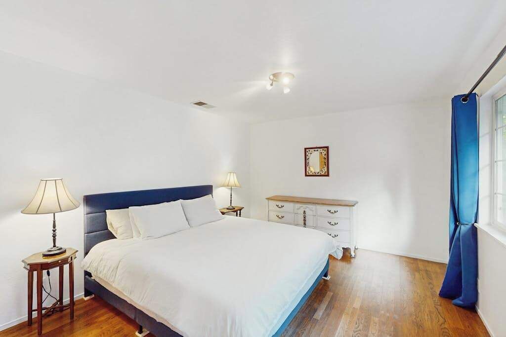 Un dormitorio con cama, lámparas de noche, cómoda y ventana con cortinas.