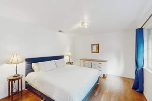 Ein Schlafzimmer mit einem Bett, Nachttischlampen, einem Schminktisch und einem Fenster mit Vorhängen.