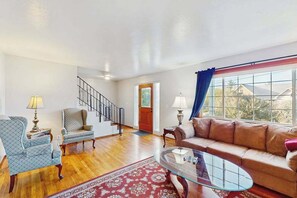 A spacious living room with a wooden floor, a glass coffee table, a sofa, and two armchairs. A staircase is visible in the background. - Eureka Charmer - Cozy Historic Getaway in the Heart of Town (Eureka)