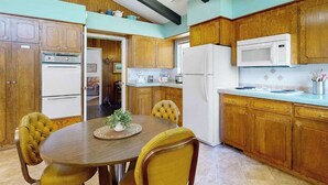 Una cocina con muebles de madera, una mesa de comedor con sillas y un refrigerador.