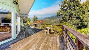 Una terraza de madera con mobiliario exterior, con vistas a un paisaje boscoso.