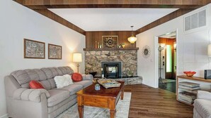 Una sala de estar con chimenea de piedra, vigas de madera en el techo, un sofá, una mesa de centro y una estantería.