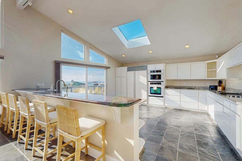 A modern kitchen with a large island, bar stools, and a skylight.