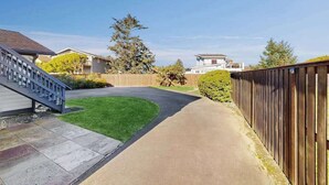 A residential driveway with a concrete path, a wooden fence, and a grassy area. - Pacific View Escape - Stunning Ocean Views & Coastal Comfort (Crescent City)