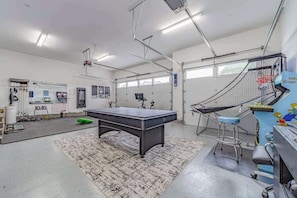 A spacious indoor area with a pool table, a bar area with stools, and a basketball hoop. - Mojo's Dojo - Unique Coastal Hideaway with a Fun, Relaxed Vibe (McKinleyville)