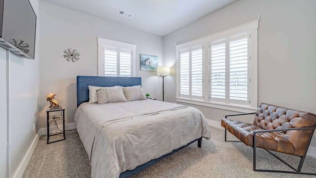 Un dormitorio con cama, una silla, una lámpara y una ventana con persianas.