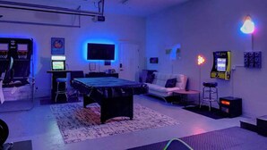 Una habitación con mesa de billar, sofá, televisor y máquinas de videojuegos.
