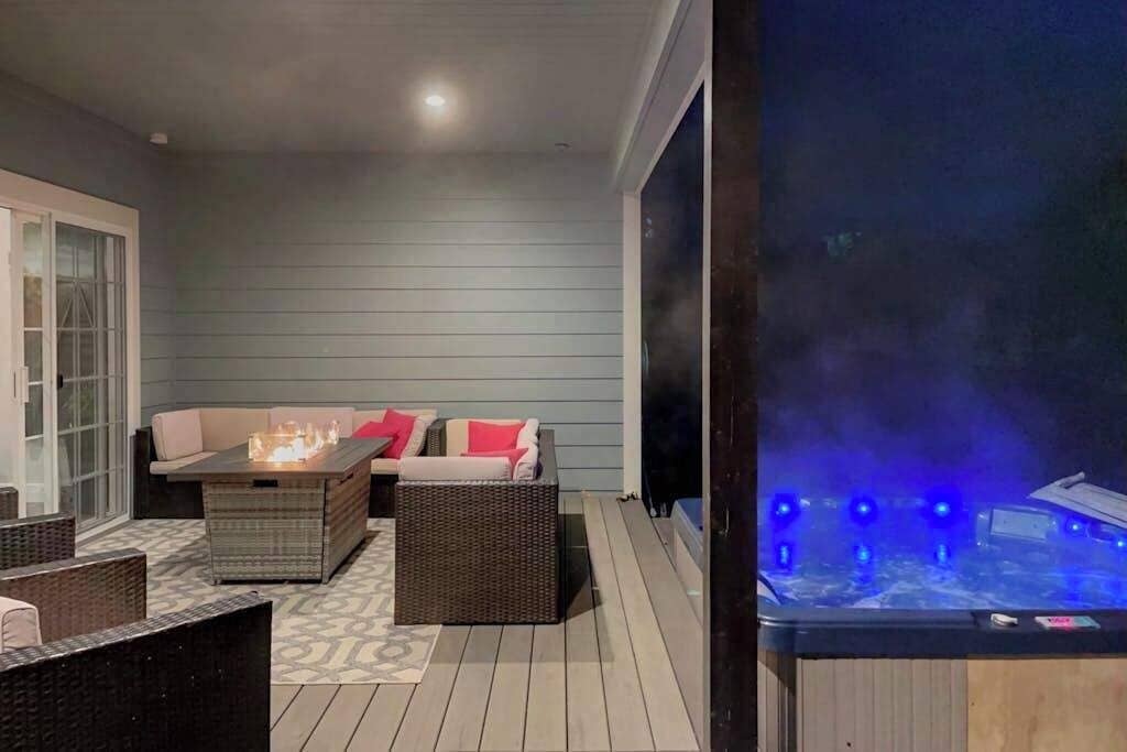 A covered outdoor area with a seating arrangement, including a sofa and a table, and a hot tub with blue lights.