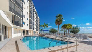 A swimming pool with lounge chairs and palm trees, adjacent to a building with balconies. - ⛱️ Coastal Views | Beachfront Location | Paradise Point–Carlos Pointe #213 🌊 (Fort Myers Beach)