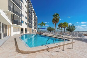 A swimming pool with lounge chairs and palm trees, adjacent to a building with balconies. - ⛱️ Coastal Views | Beachfront Location | Paradise Point–Carlos Pointe #213 🌊 (Fort Myers Beach)