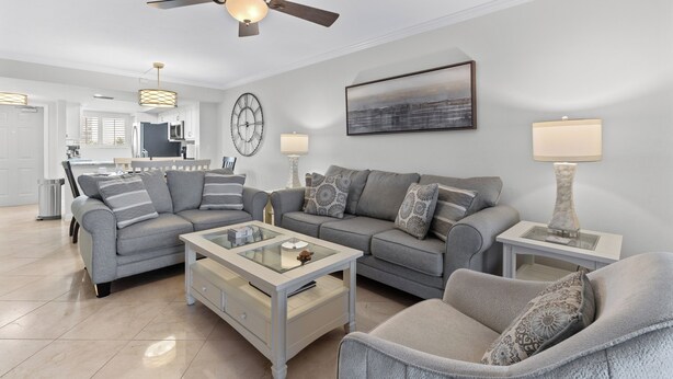 A modern living room with a ceiling fan, a dining area, and a kitchen in the background. - ⛱️ Coastal Views | Beachfront Location | Paradise Point–Carlos Pointe #213 🌊 (Fort Myers Beach)