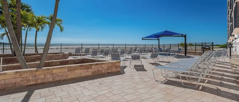 Ein Poolbereich auf dem Dach mit Liegestühlen, einem blauen Sonnenschirm und Palmen.