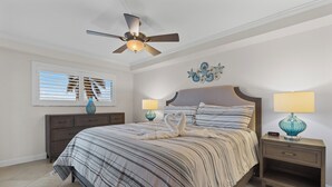 A bedroom with a bed, two bedside tables, a ceiling fan, a window with blinds, and a wall decoration. - ⛱️ Coastal Views | Beachfront Location | Paradise Point–Carlos Pointe #213 🌊 (Fort Myers Beach)