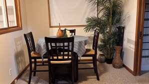 A dining area with a table set for four, surrounded by chairs, a potted plant, and a window.