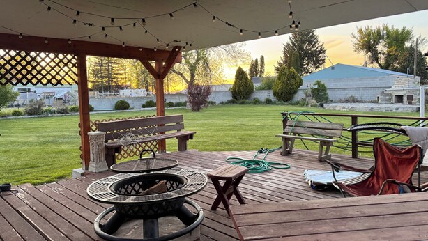 A covered outdoor patio with a fire pit, wooden benches, and string lights.