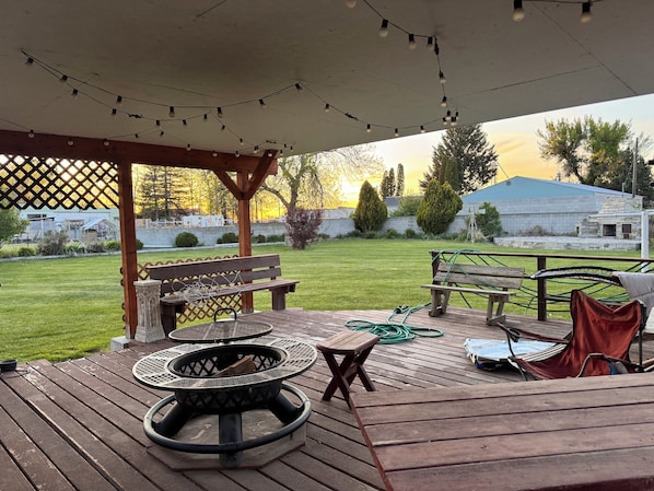 A covered outdoor patio with a fire pit, wooden benches, and string lights.
