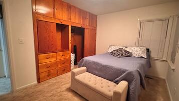 Un dormitorio con cama, un banco, un armario y una ventana.