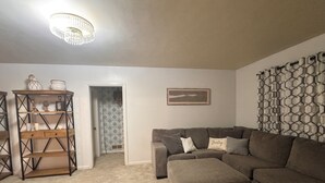 A living room with a sectional sofa, a wooden console table, a chandelier, and a patterned wall.