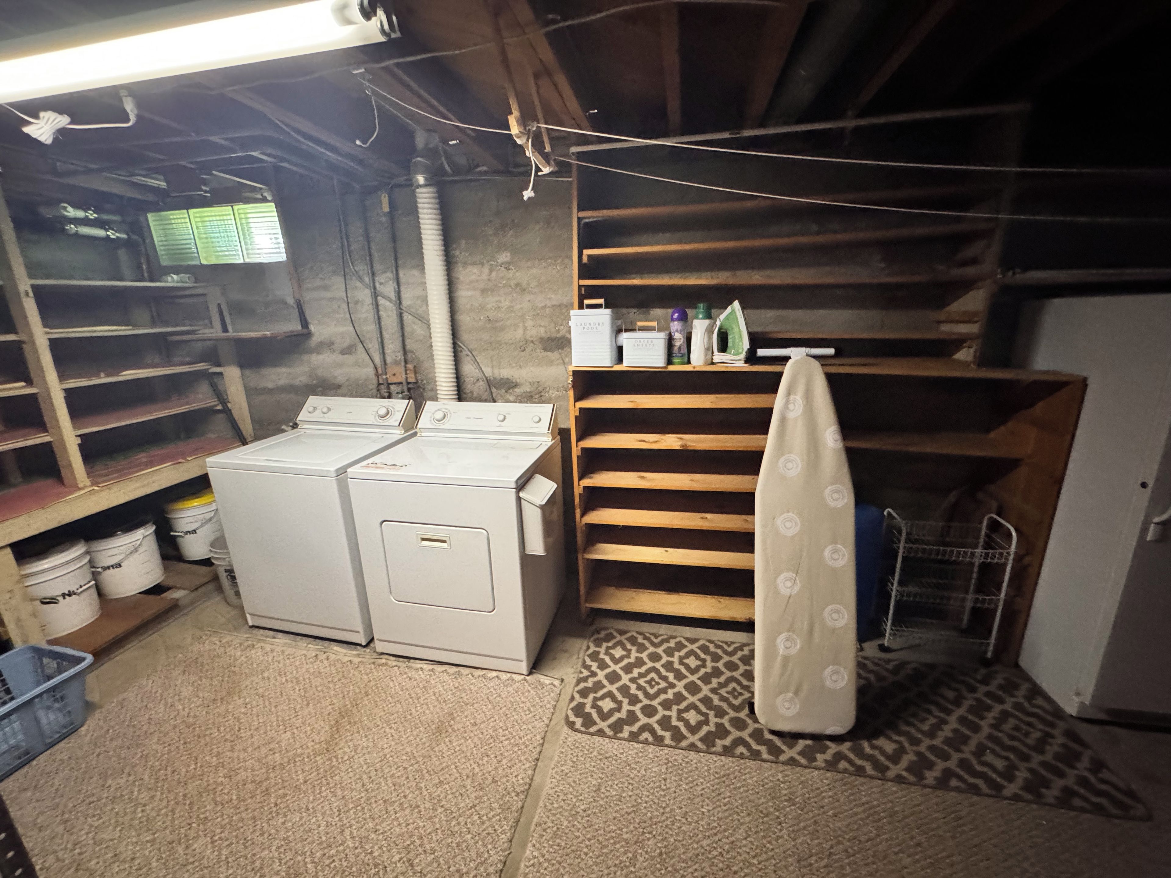 A laundry room with two washing machines, shelves with cleaning supplies, and a patterned rug.