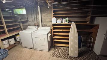 A laundry room with two washing machines, shelves with cleaning supplies, and a patterned rug.