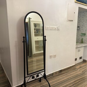 A mirror with a stand, a white cabinet with glass doors, and a bathroom with a countertop and sink. - Cozy 3 BHK in Kadavanthra (Ernakulam)