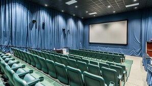 En teatersal med rækker af grønne sæder, et stort lærred og blå gardiner.