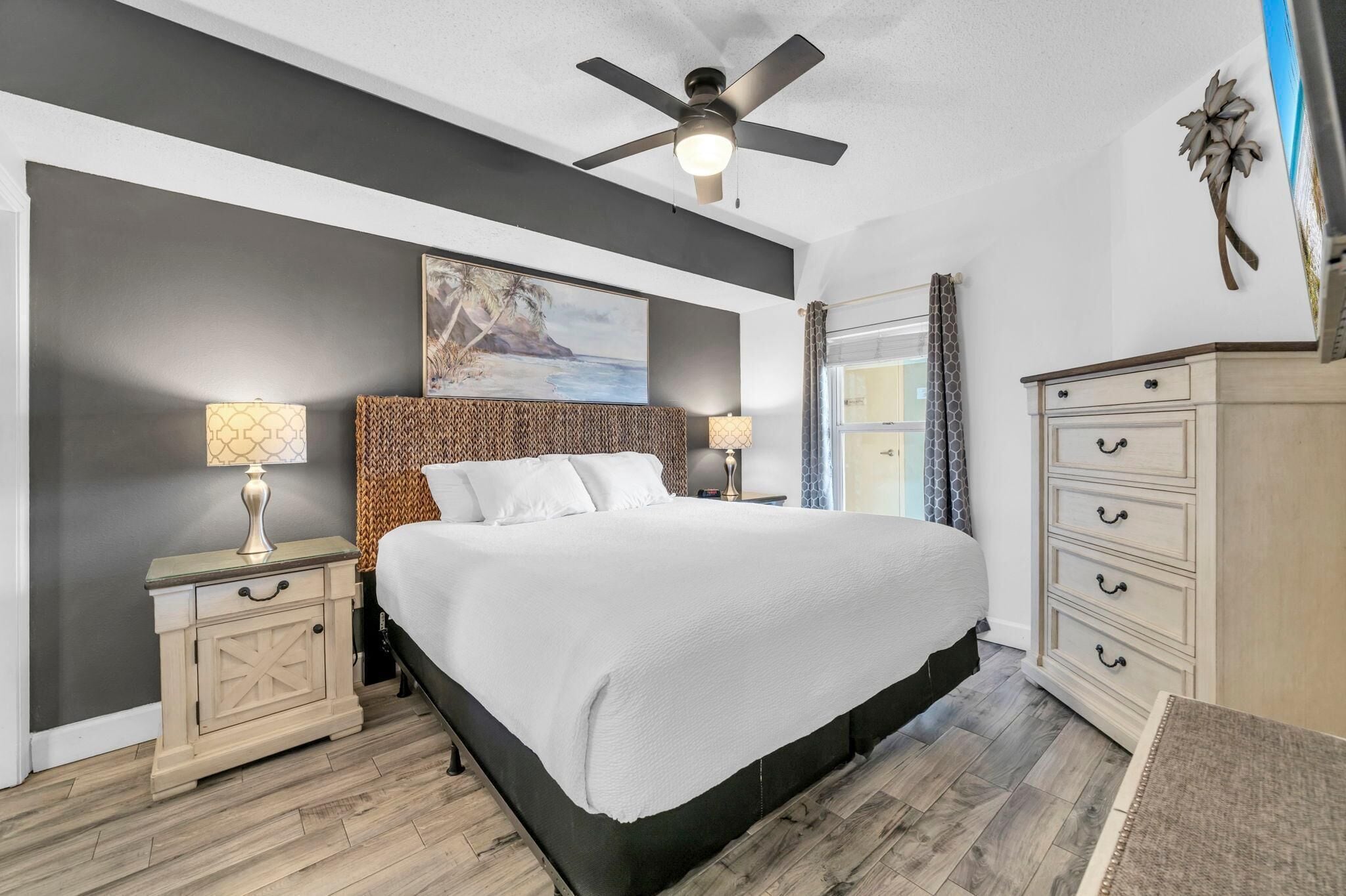 A bedroom with a bed, nightstands, a dresser, a ceiling fan, and a painting on the wall.