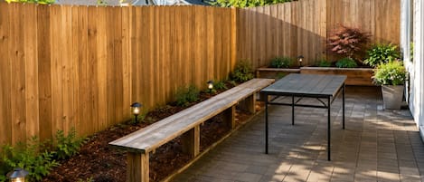A wooden deck with a bench and table, surrounded by a wooden fence and potted plants.