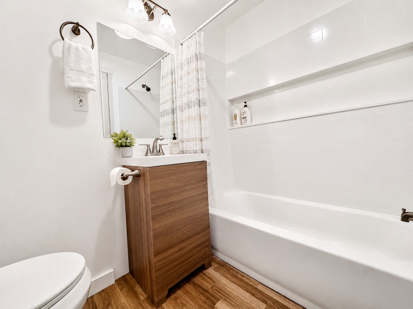 Een moderne badkamer met een wit toilet, een houten wastafelmeubel, een wastafel met spiegel en een bad.