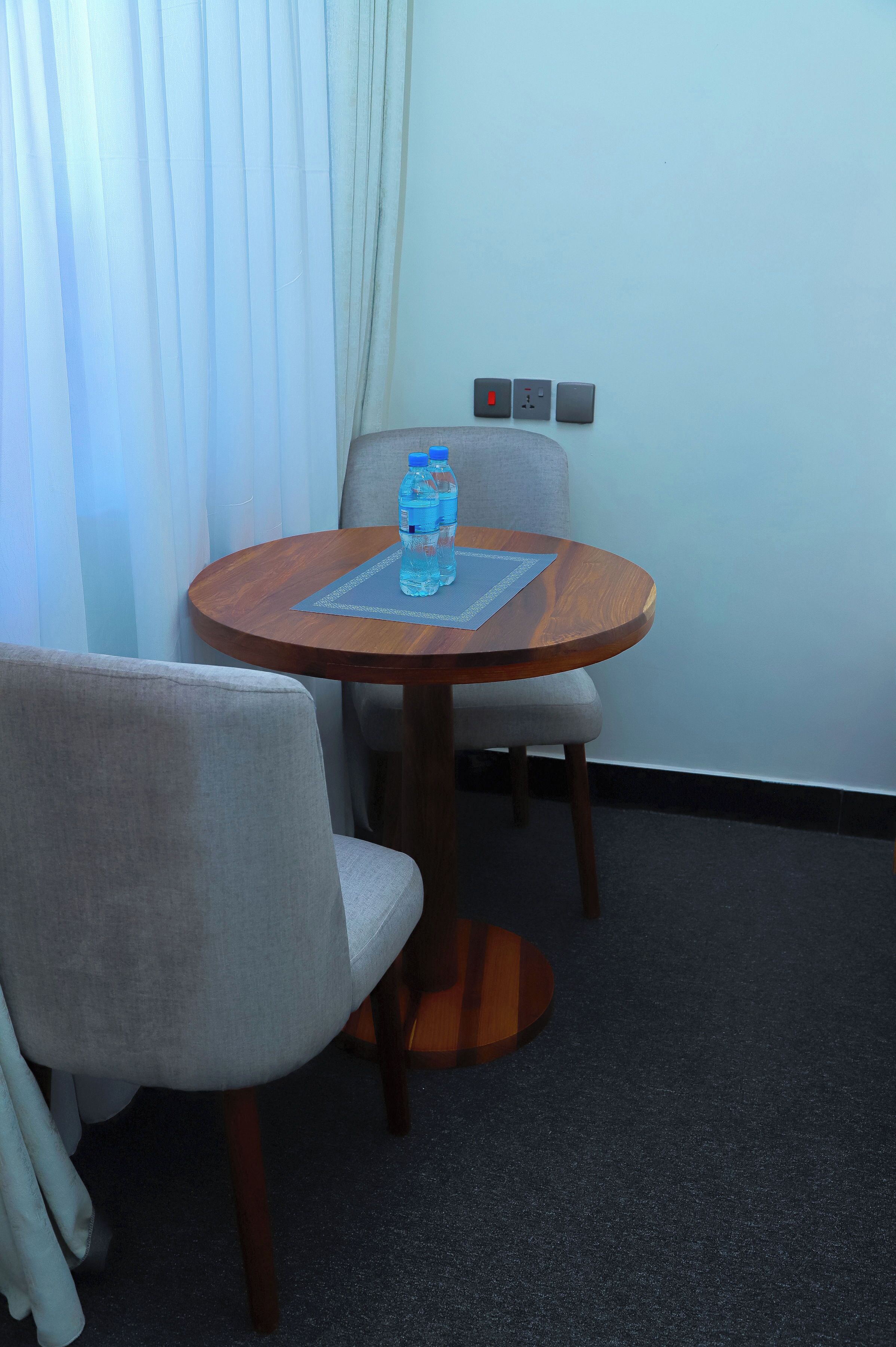 A small round table with two chairs, a water bottle, and a power outlet on the wall.